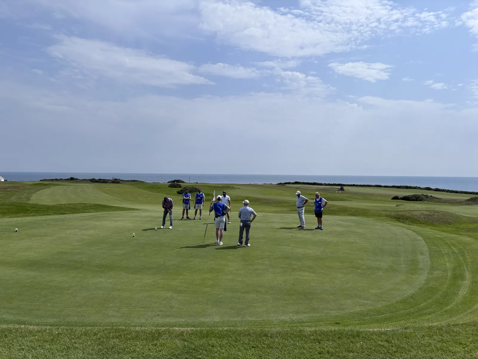 Golfers and caddies on a green at Ardglass Golf Club, Northern Ireland, with pints of Guinness on the green and the Irish Sea behind